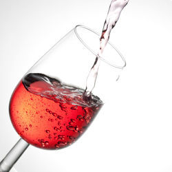 Close-up of red wine pouring in glass against white background