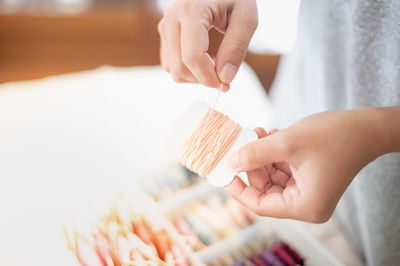 Close up hands of tailor woman holding beige threads and different colors in the box.