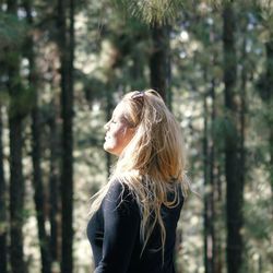 Side view young woman standing against trees in forest