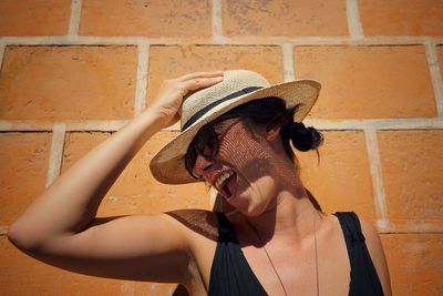 Cheerful woman wearing hat against brick wall