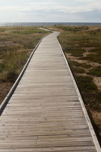 Boardwalk leading towards landscape against sky