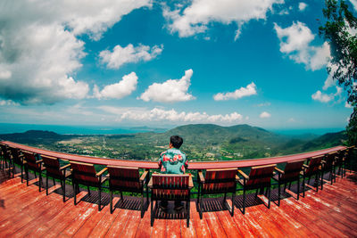 Rear view of woman sitting on bench against sky