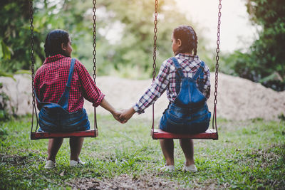 Friends holding hands while sitting on swing at park
