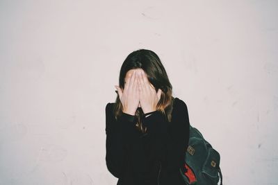 Woman covering face with hands standing against wall