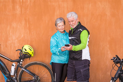 Couple with bicycle standing against wall