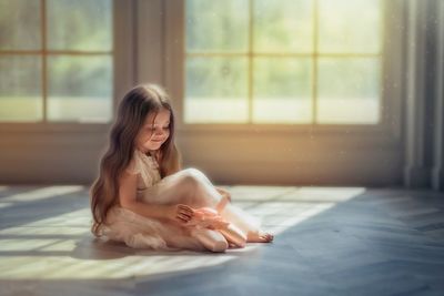 Full length of cute smiling girl with ballet shoes sitting on floor