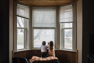 Rear view of siblings kneeling by window at home