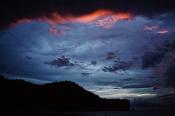 Scenic view of silhouette cliff by sea against cloudy sky during sunset