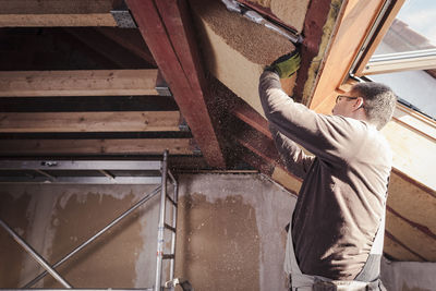 Roof insulation, worker filling pitched roof with wood fibre insulation