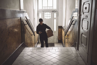 Delivery man with package using mobile phone against door