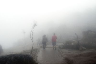 People walking on snow covered landscape in foggy weather