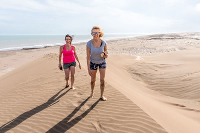 Frontal view of two women walking on top of a large dune. mother and daughter