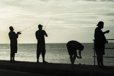 Silhouette people fishing in sea against sky