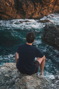 Rear view of man sitting on rock at beach