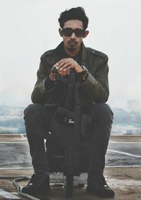 Full length of young man with gun on terrace against sky