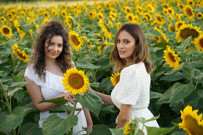 Portrait of smiling friends standing on sunflower field against sky