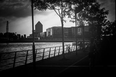 Silhouette buildings by river against sky in city