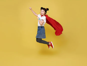 Full length of a young woman jumping over yellow background