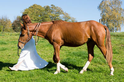 Side view of young woman with horse walking on grassy field against sky