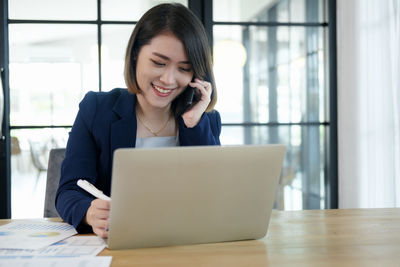 Mid adult woman using phone while sitting on table