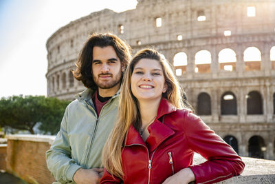 Young couple traveling to rome. the couple is posing for a photo in front of the colosseum.