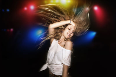Woman with blond hair dancing against illuminated multi colored lights at garden party