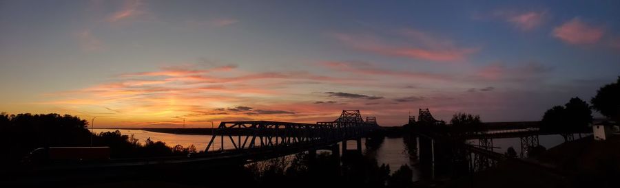 Silhouette bridge over river against sky during sunset