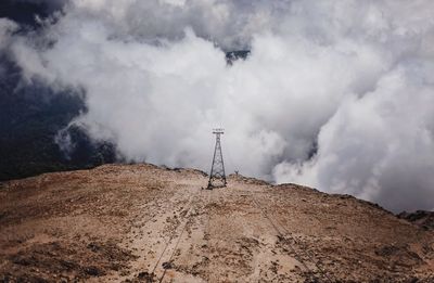 Electricity pylon on landscape against cloudy sky