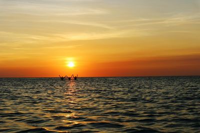 Silhouette man in sea against sky during sunset