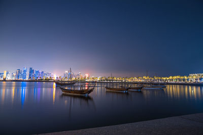 Illuminated city by river against sky at night