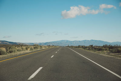 Empty road by mountains against sky