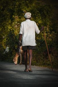 Rear view of woman with dog walking on road