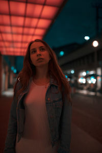 Young woman standing under illuminated lights on footpath at night