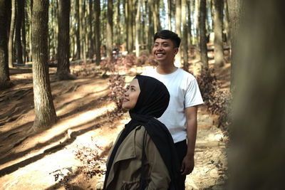 Happy woman standing by tree trunk in forest