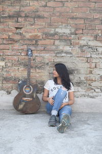 Full length of young woman sitting on brick wall