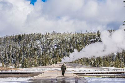 Man walking on snow covered field against sky