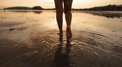 Low section of woman walking at beach during sunset