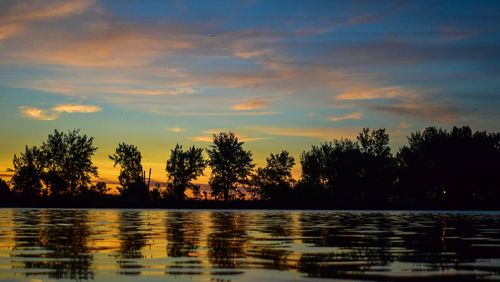 Silhouette trees by lake against sky during sunset