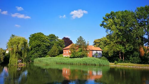 Trees by lake and buildings against sky