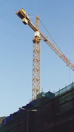 Low angle view of crane against clear blue sky