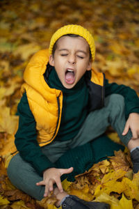 Portrait of a fashionable child boy autumn sitting on a trail in orange leaves in the afternoon