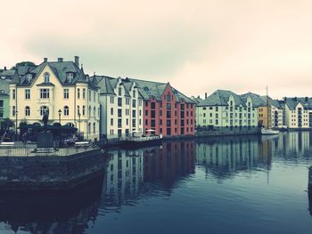 Buildings by canal against sky during sunset