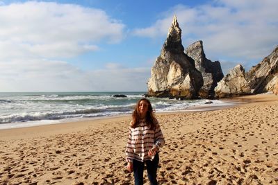 Portrait of smiling woman standing at sandy beach against sky