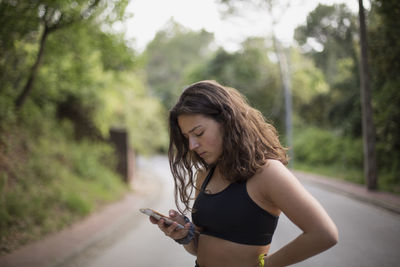 Young woman looking at camera while standing on mobile phone