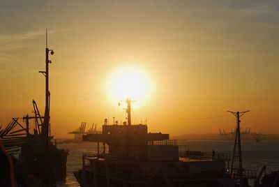 Silhouette cranes at harbor against sky during sunset