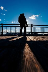 Silhouette man on footbridge against sky in city