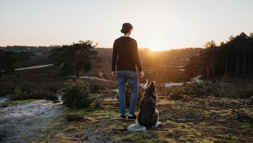 Rear view of woman with dog against sky during sunset