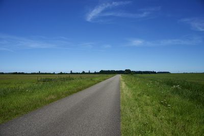 Road amidst field against blue sky