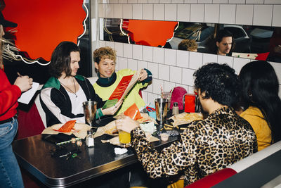 Male and female friends talking ordering food to waitress while sitting at table in cafe