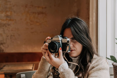 Beautiful young woman taking photos with vintage film camera indoor.